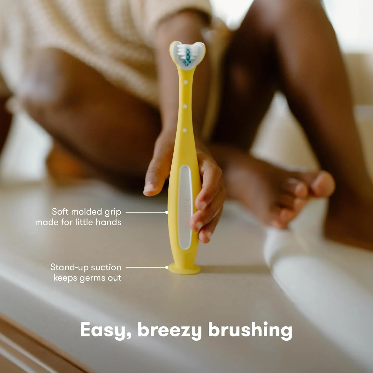 A Frida Baby Toothhugger toothbrush in yellow and blue, designed with a triple-angle brush head for cleaning all sides of a toddler's teeth simultaneously.