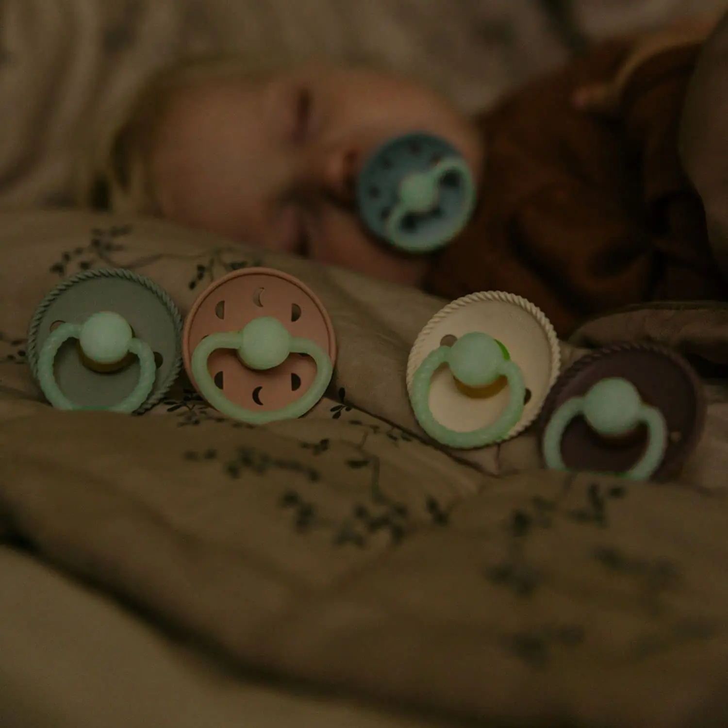 Two-pack of FRIGG Rope pacifiers in cream and stone blue with glow-in-the-dark handles and round, latex-free silicone nipples, designed to mimic breastfeeding.