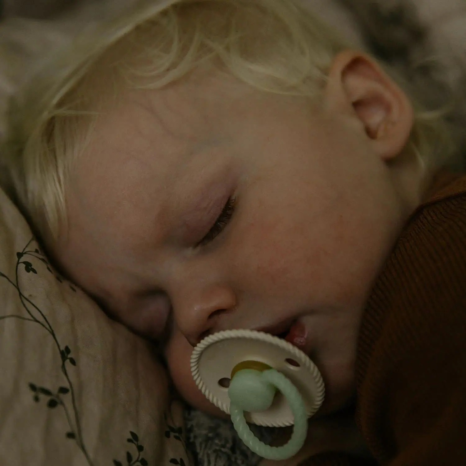 Two-pack of FRIGG Rope pacifiers in cream and stone blue with glow-in-the-dark handles and round, latex-free silicone nipples, designed to mimic breastfeeding.