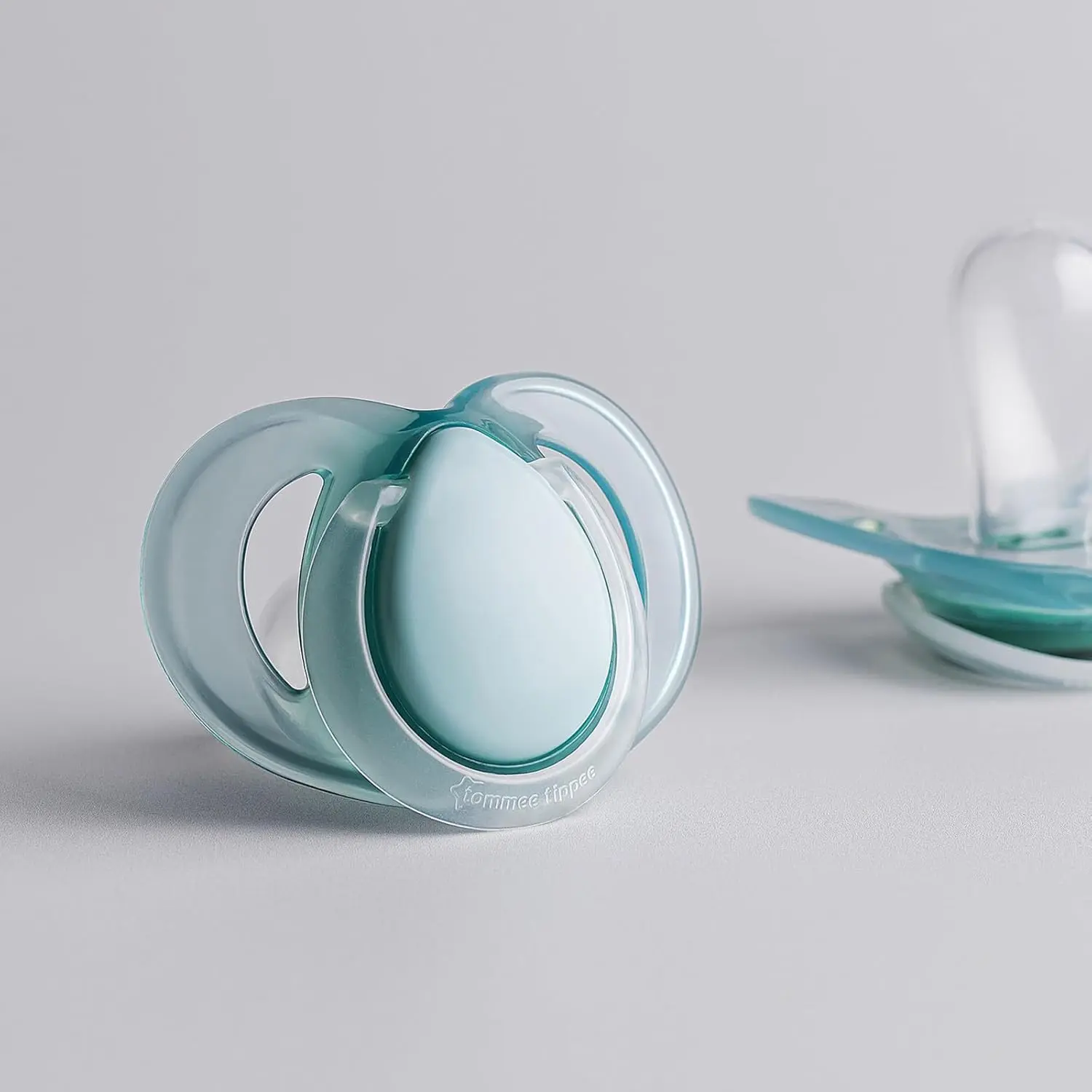 This image shows a 2-pack of Tommee Tippee nighttime pacifiers designed for babies 0-6 months, featuring a glow-in-the-dark design, symmetrical nipple, and a curved shield for comfort and skin protection.