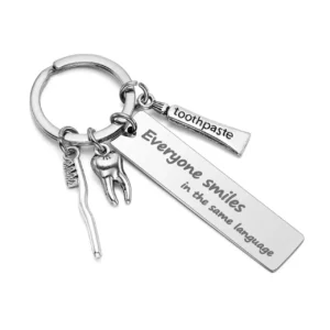 Stainless steel keyring with a tooth, toothbrush, and toothpaste charm, engraved with 'Everyone smiles in the same language,' perfect as a dentist gift.